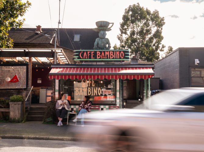 cafe bambino storefront with a baby that has a cup on its head on top of the buliding with a speeding car in front of it
