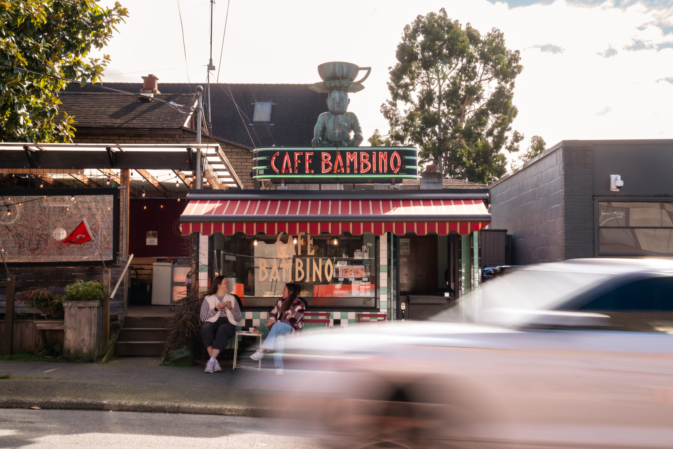 cafe bambino storefront with a baby that has a cup on its head on top of the buliding with a speeding car in front of it