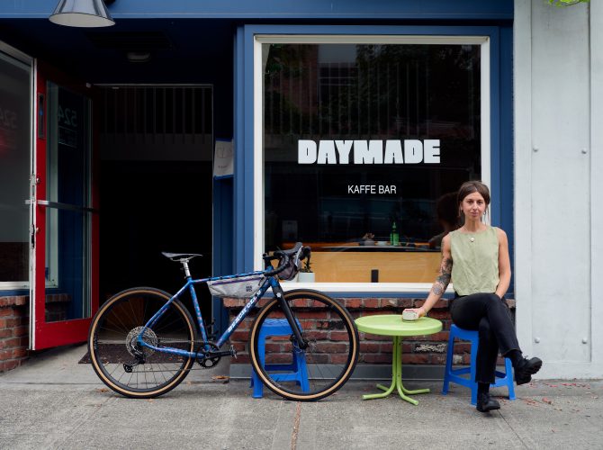 the front of a cafe witha woman sitting at a table next to her bike