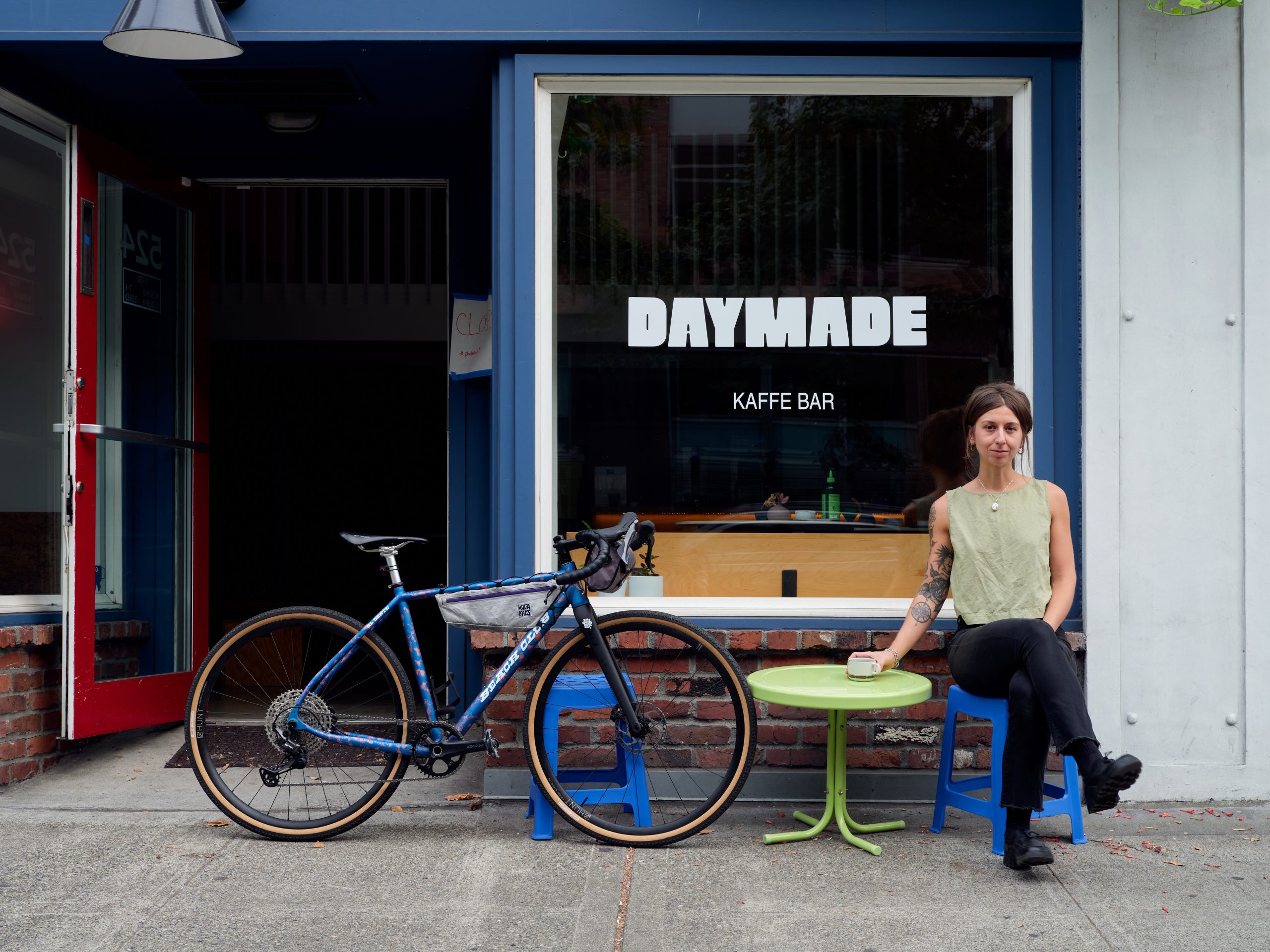 the front of a cafe witha woman sitting at a table next to her bike